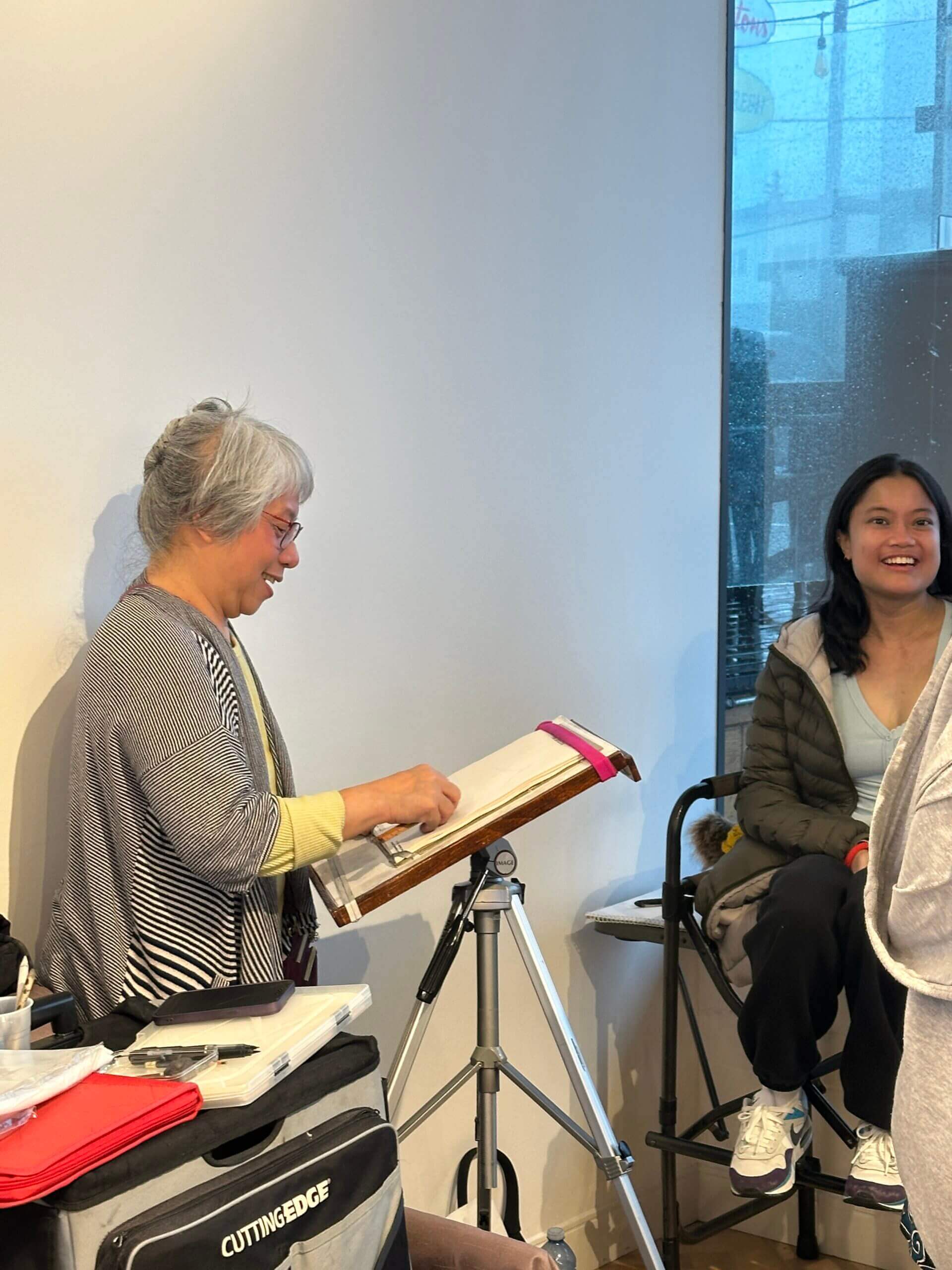 Artist sketching woman on chair beside window